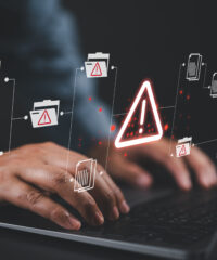 Warning alert icon with a hacked document system.Man typing on a keyboard with a red cybersecurity threat alert, surrounded by digital files and documents.